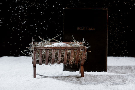 Manger with baby Jesus, hay and Holy Bible on snow against dark backgroundの写真素材
