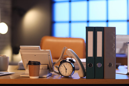 Alarm clock with folders, telephone and coffee cup on table in office at night. Deadline conceptの写真素材