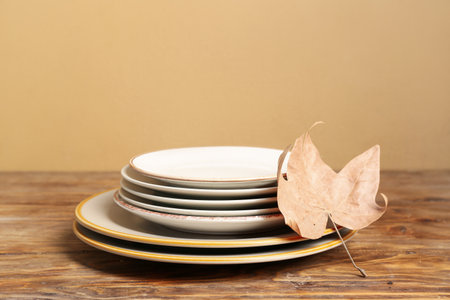 Stack of dishes with autumn leaf on table against beige backgroundの写真素材