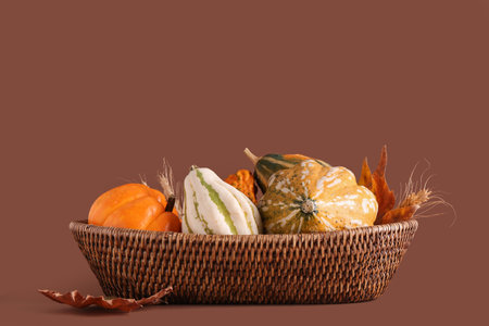 Wicker bowl with fresh pumpkins, wheat and autumn leaves on brown backgroundの写真素材