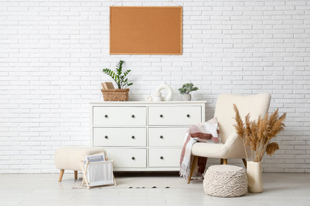Armchair, pouf, pampas grass, frame and chest of drawers near white wall in roomの写真素材