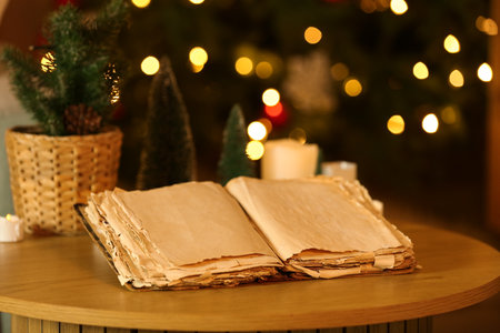 Opened old book, Christmas decorations and candles on table in dark room with glowing lights, closeup. Christmas story conceptの写真素材