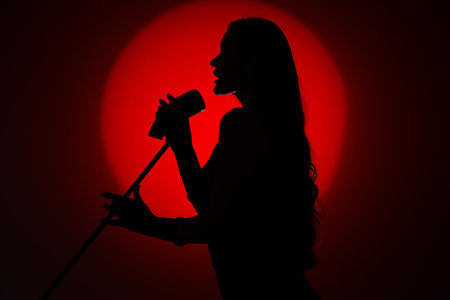 Silhouette of female singer with microphone on dark red backgroundの写真素材