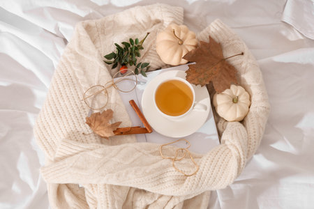 Composition with cup of green tea, notebook, sweater and autumn leaves on light fabric as backgroundの写真素材