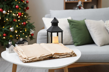 Opened old book and glowing lantern on table in living room, closeup. Christmas story conceptの写真素材