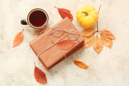 Composition with stack of books, cup of tea and autumn leaves on light grunge background
