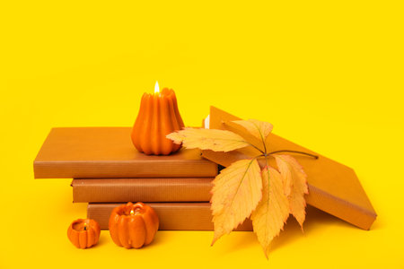 Stack of books, autumn leaves and burning candles on yellow backgroundの写真素材