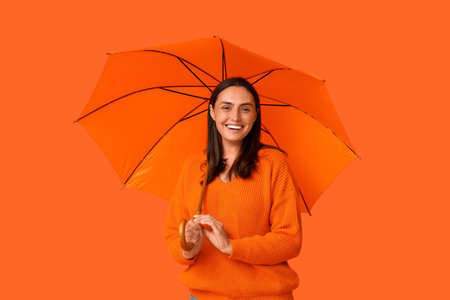 Happy young woman with umbrella on orange backgroundの写真素材
