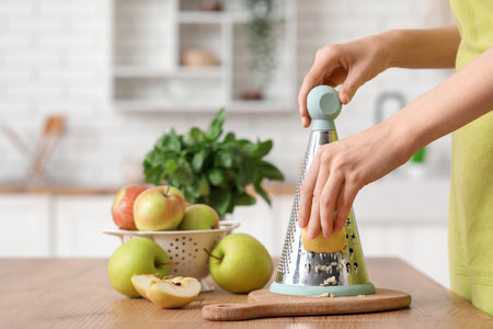 Young woman grating fresh apple in kitchenの写真素材