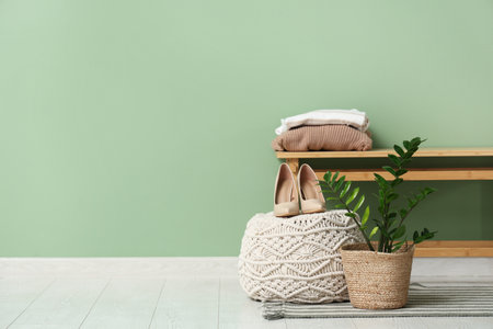 Bench with houseplant, clothes, pouf and shoes near green wall in roomの写真素材