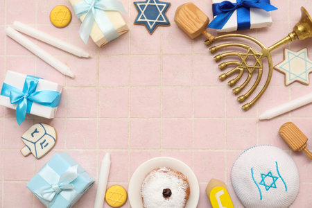 Frame made from menorah, candles, donut and gift boxes on pink tiled background. Hanukkah celebrationの写真素材