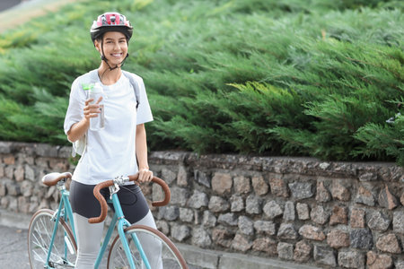 Sporty young woman with bicycle and bottle of water on city streetの写真素材