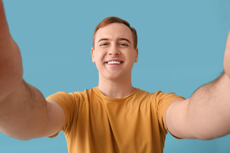 Young man taking selfie on blue background, closeup