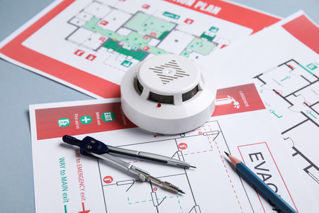 Modern smoke detector with pair of compasses and evacuation plans on gray background, closeupの写真素材