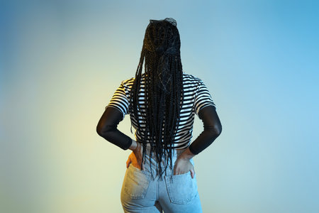 Cool young African-American woman with braids on color background, back viewの写真素材