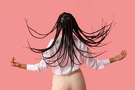 Stylish young African-American woman with braids on pink background, back view