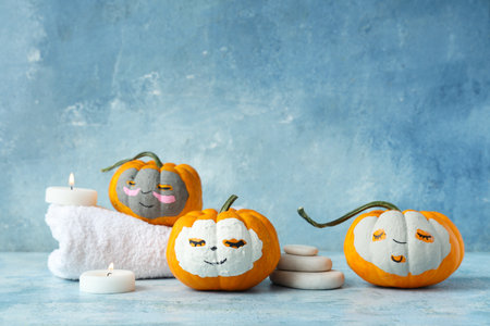 Pumpkins with drawn faces, clay masks, towel, spa stones and candles on blue grunge backgroundの写真素材
