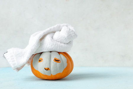Pumpkin with drawn face, clay mask and towel on blue table near white wallの写真素材