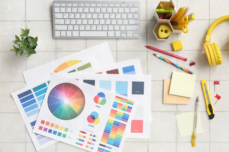 Workplace of graphic designer with keyboard, stationery and color charts on white tiled table
