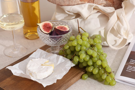 Wooden board with sweet ripe grapes, camembert cheese, figs, baguette and bottle of wine on white backgroundの写真素材