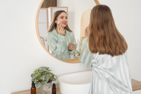 Young woman massaging her face with tool near mirror in bathroomの写真素材