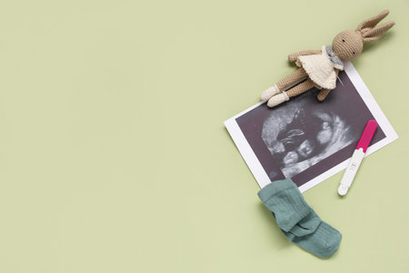 Composition with baby socks, sonogram image, toy rabbit and pregnancy test on green backgroundの写真素材
