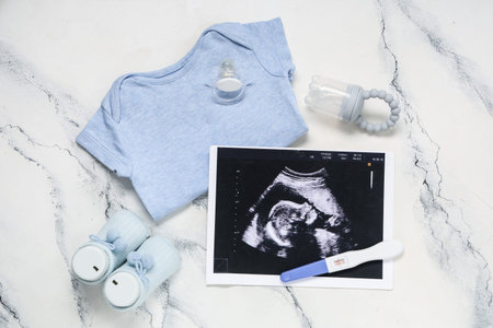 Composition with baby clothes, sonogram image, pregnancy test and nipples on grunge white background
