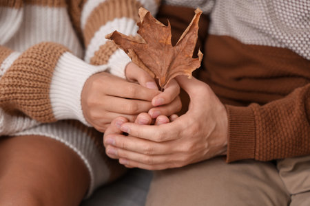 Young couple with autumn leaf sitting at home, closeupの写真素材