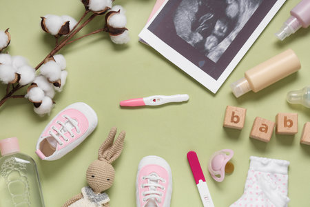 Frame made of shoes, sonogram image, pregnancy tests and bottles of cosmetic products on green...