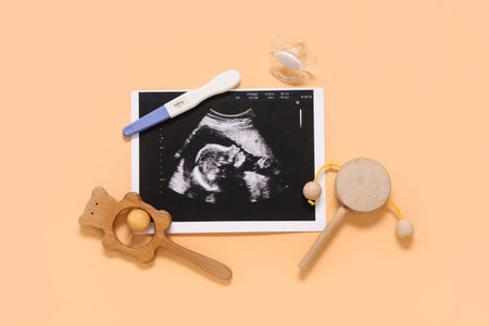 Composition with baby rattles, sonogram image, pregnancy test and nipple on orange background