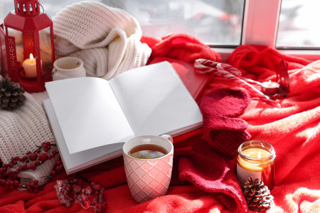 Beautiful composition with books, cup of tea, Christmas decorations and warm clothes on windowsillの写真素材