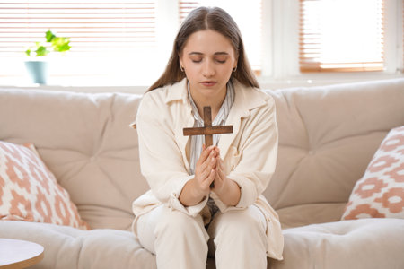 Young woman praying with beads on sofa at home