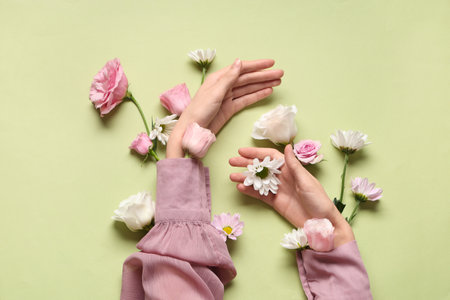 Female hands with different fresh flowers on light green background. Care conceptの写真素材