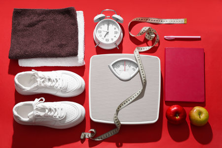 Scales with measuring tape, sneakers and alarm clock on red background. Weight loss conceptの写真素材