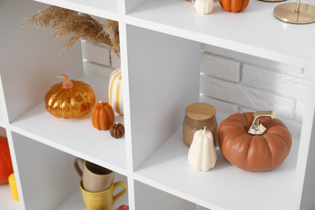 Shelving unit with candles in shape of pumpkin and glass pumpkins near white brick wallの写真素材