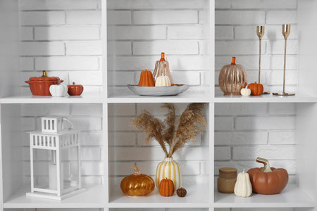 Shelving unit with candles in shape of pumpkin and decorations near white brick wallの写真素材