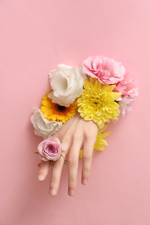 Female hand with different fresh flowers visible through hole in pink paperの写真素材