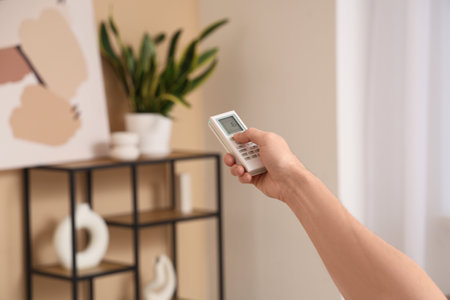 Male hand with air conditioner remote control in living roomの写真素材