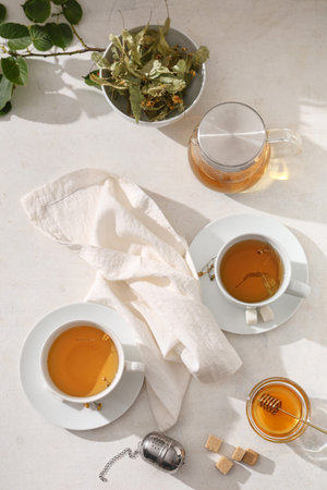 Cups of tasty linden tea with teapot, honey and leaves on white background