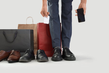 Businessman in new shoes with credit card and mobile phone on light background