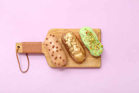 Wooden board with delicious glazed eclairs on color backgroundの写真素材