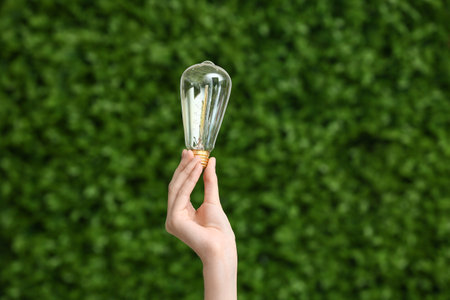 Woman with light bulb outdoors, closeup. Green Energy conceptの写真素材