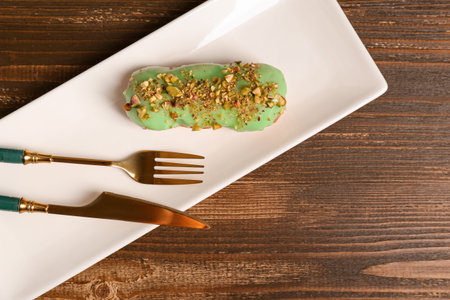 Plate with sweet eclair on wooden background