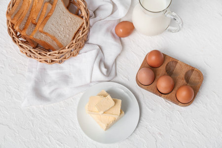 Composition with fresh butter, chicken eggs and bread on light background