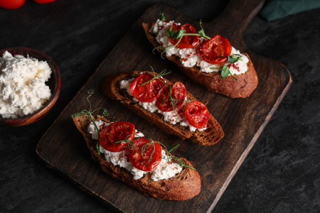 Wooden board of tasty tomato bruschetta with ricotta on black backgroundの写真素材