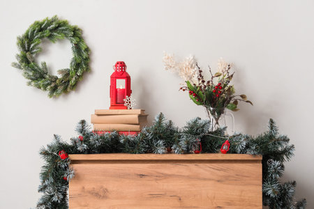 Lantern with burning candle and Christmas decor on table near white wall at home