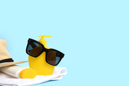 Sunglasses, hat, bottle of sunscreen cream and towel on blue background