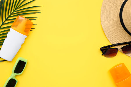Composition with bottles of sunscreen cream, hat and sunglasses on yellow background