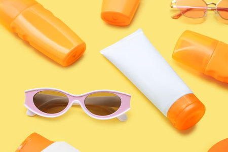 Composition with bottles of sunscreen cream and sunglasses on yellow background, closeup