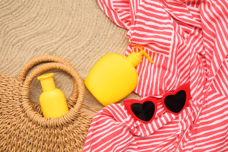 Bag, sunglasses and bottles of sunscreen cream on sand as background